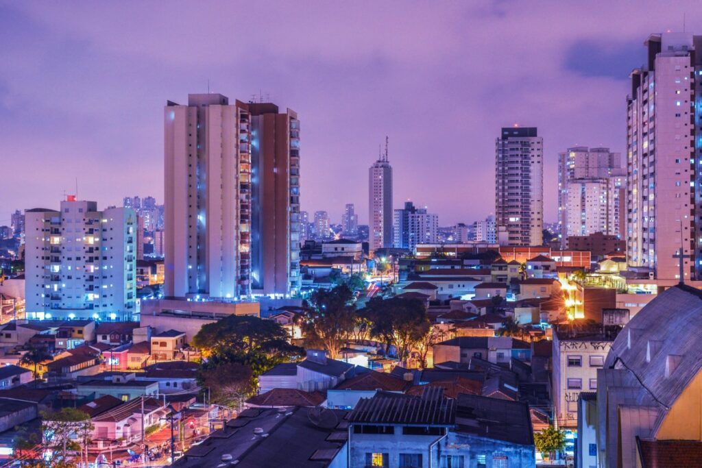 Imagem da paisagem urbana de uma cidade brasileira à noite, com prédios altos iluminados e as casas mais baixas na parte inferior. Incluindo: Perspectivas do Marketing de Mídias Sociais no Brasil em 2025