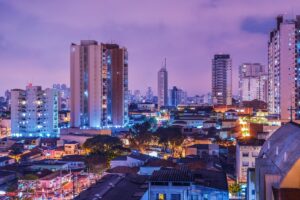 Imagem da paisagem urbana de uma cidade brasileira à noite, com prédios altos iluminados e as casas mais baixas na parte inferior. Incluindo: Perspectivas do Marketing de Mídias Sociais no Brasil em 2025