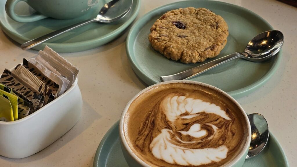 A cozy coffee setting with a latte featuring latte art,an oatmeal cookie,and a bowl of sugar packets."A Tentativa da Byte App de Derrubar o TikTok:Uma Análise Completa",reflecting on the app's strategy to challenge social media giants.